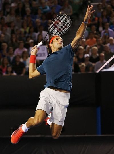 a male tennis player is jumping in the air with his racquet raised up