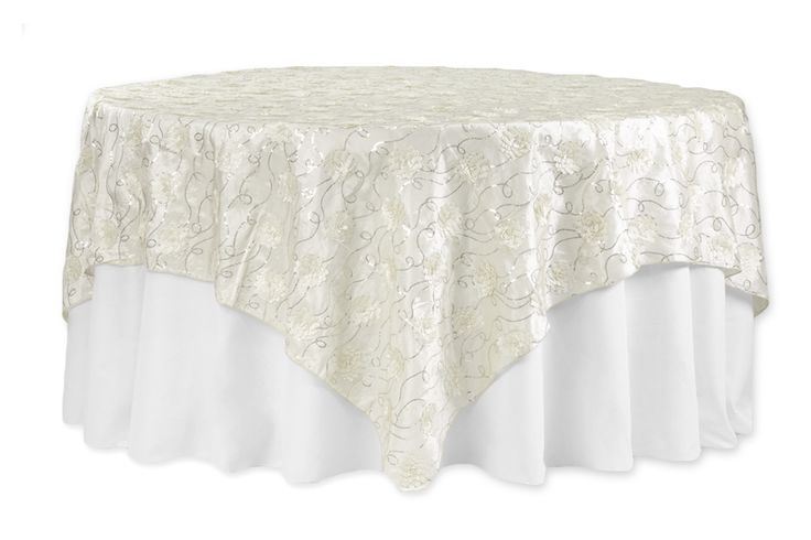 a round table with white linens on it and a gold floral design over the top