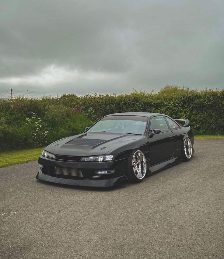 a black sports car parked on the side of a road next to grass and bushes