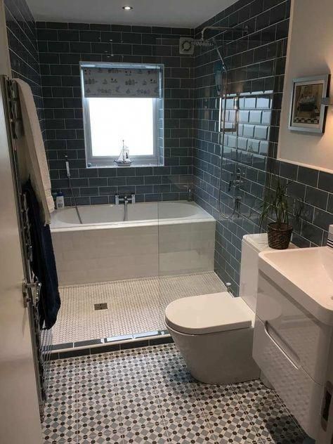 a white toilet sitting next to a bath tub in a bathroom under a window with blue tiles on the floor