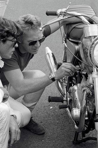 a man and woman sitting next to each other on the ground near a parked motorcycle