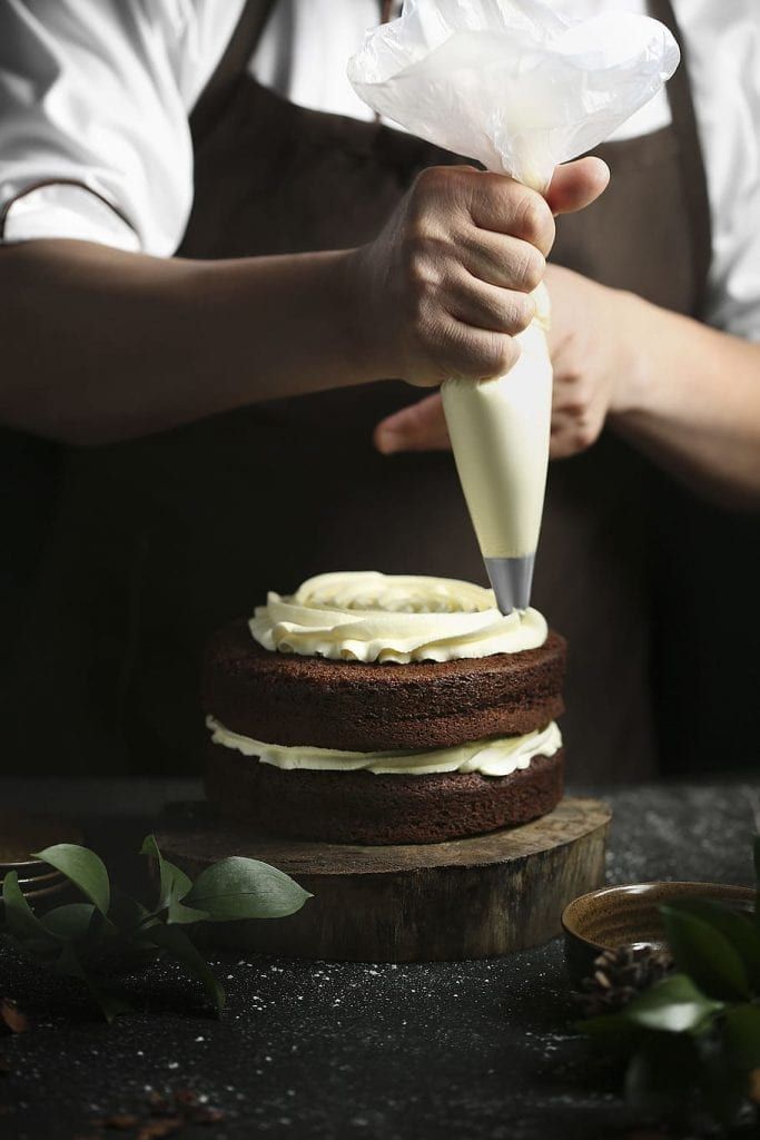 a baker is decorating a cake with icing and frosting on the table