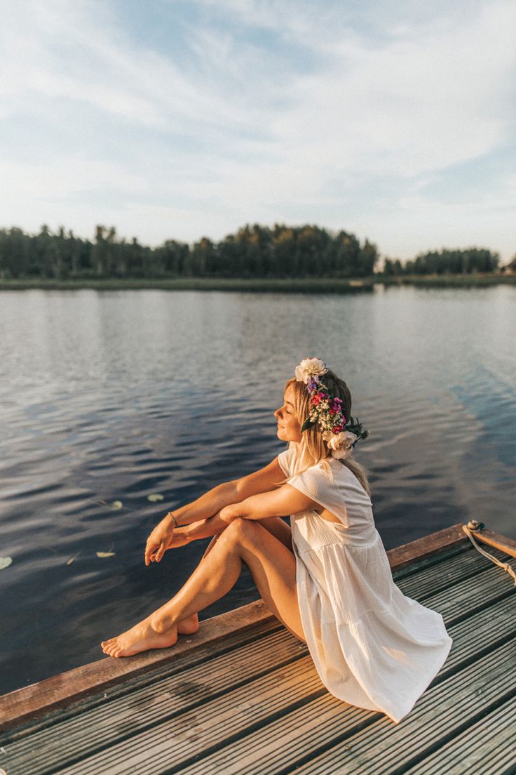 a woman sitting on the end of a wooden dock next to a body of water