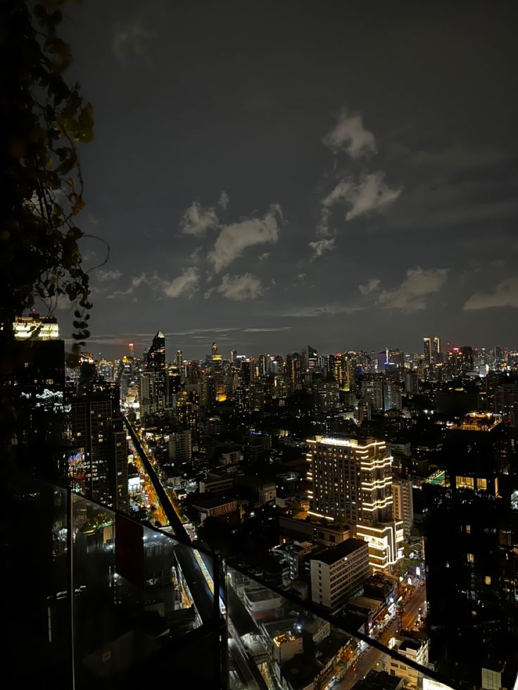 the city is lit up at night with clouds in the sky and lights on buildings