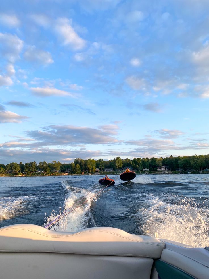 two people on jet skis being pulled by a boat in the water with trees in the background