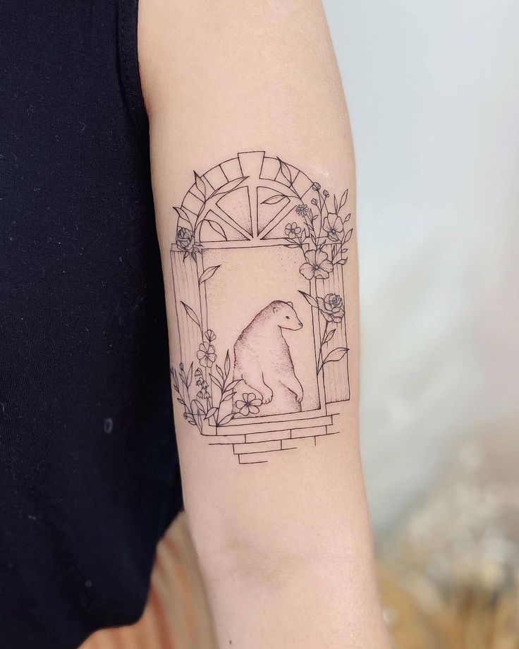 a woman's arm with a bear and flowers tattoo on the left side of her arm