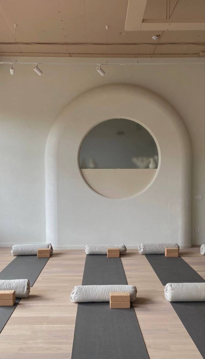 yoga mats lined up on the floor in front of a round window with circular mirror