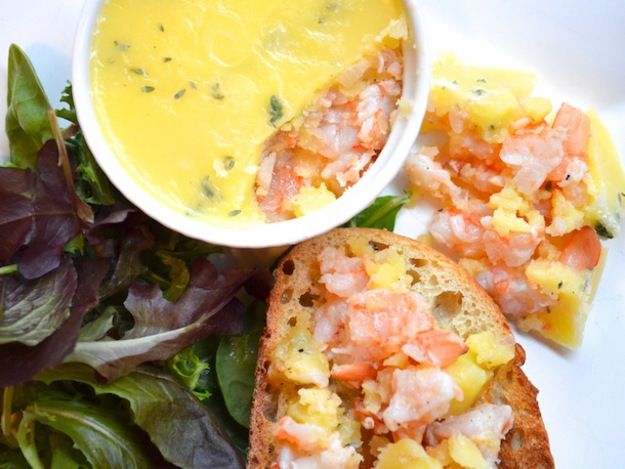 two pieces of bread with shrimp on them next to a bowl of soup and salad