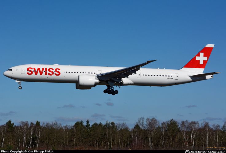 an airplane is flying in the sky over some trees and grass with its landing gear down