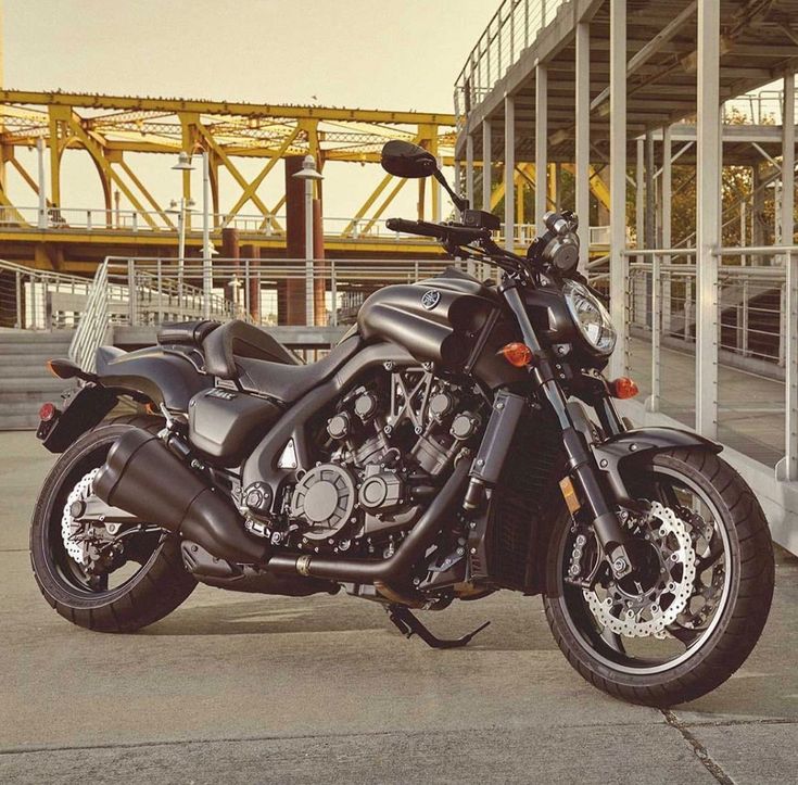 a black motorcycle parked in front of a large metal structure with yellow beams behind it