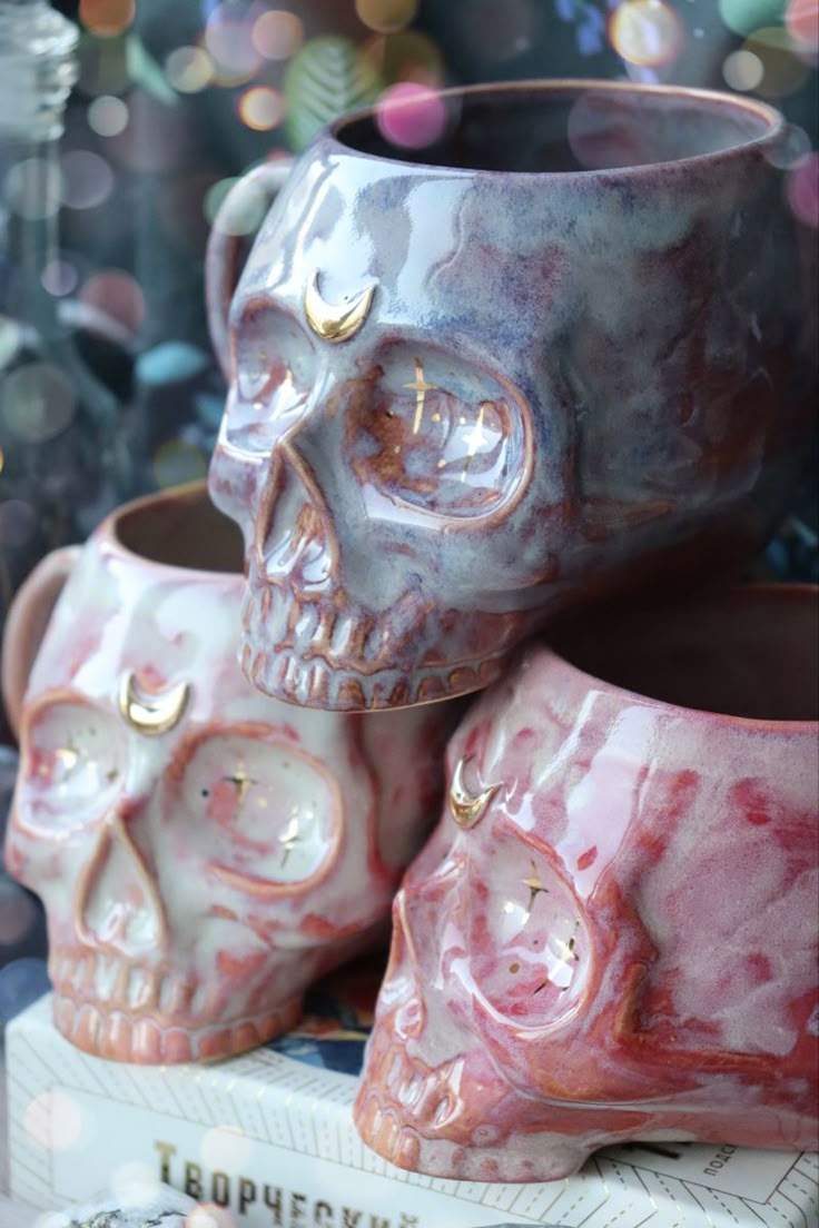 two skull mugs sitting next to each other on top of a book with lights in the background