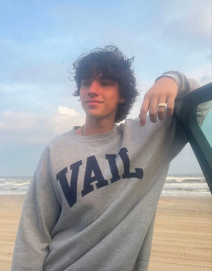 a young man is standing on the beach with his car door open and looking at the camera