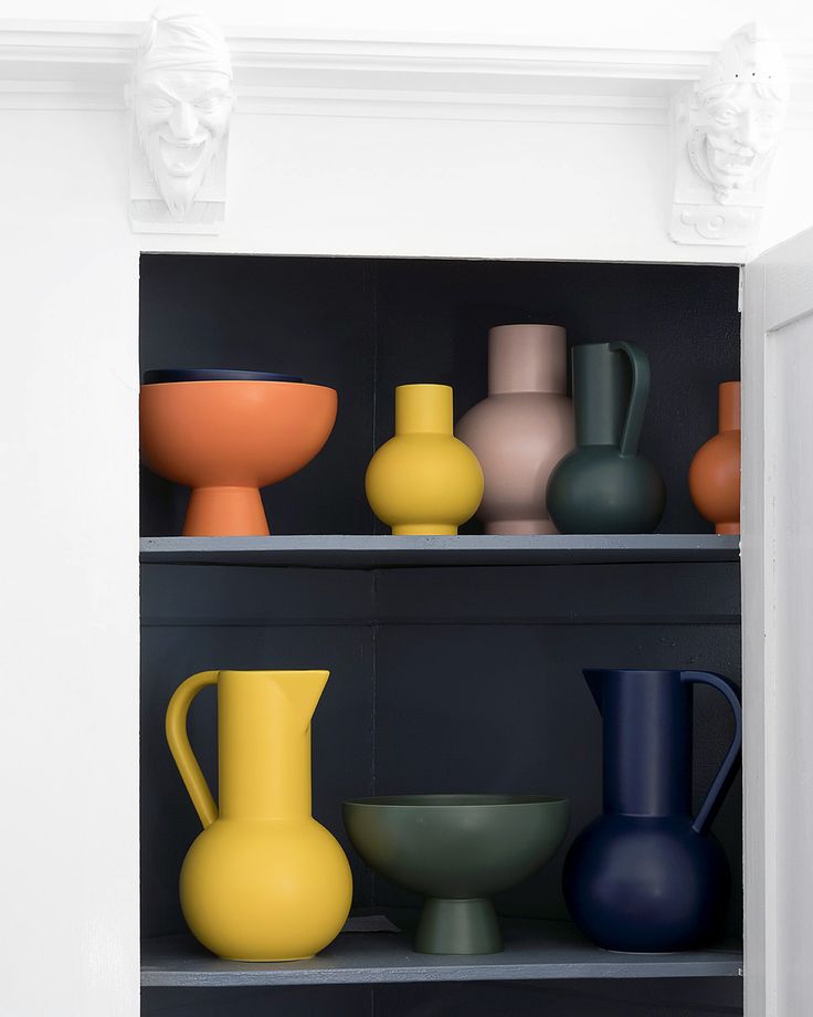 several different colored vases on shelves in a room with black walls and grey shelving