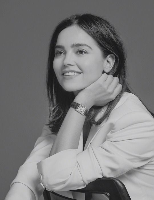 a black and white photo of a woman with her hand on her shoulder smiling at the camera