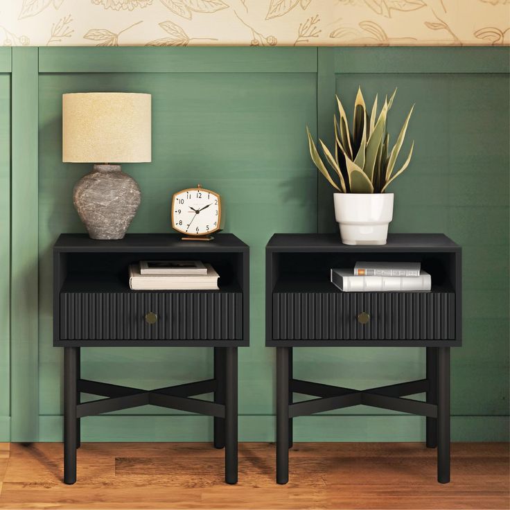 two black nightstands with plants and a clock on each end table in front of a green wall