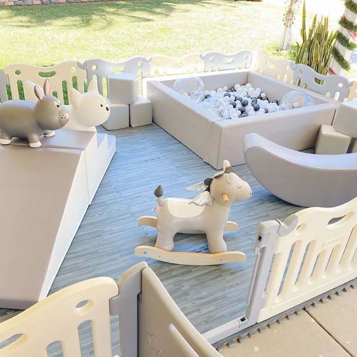 an outdoor play area with white furniture and toys on the ground, including a rocking horse