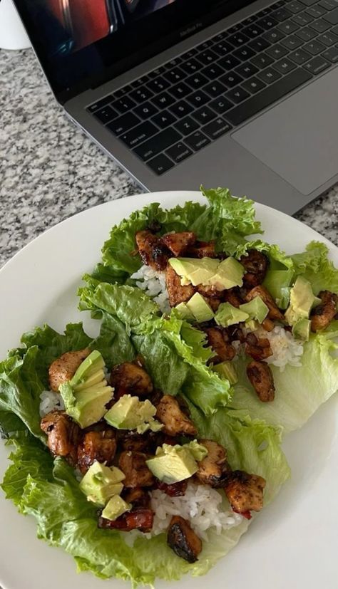 two lettuce wraps with chicken and avocado are on a plate next to a laptop