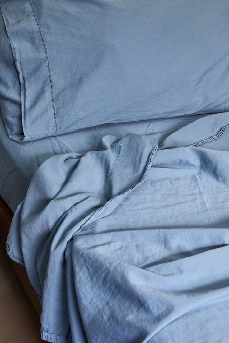 an unmade bed with blue sheets and pillows