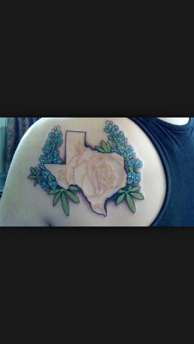 the back of a woman's shoulder with flowers and state tattoos on it,