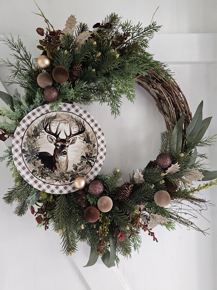 a christmas wreath hanging on the wall with a deer plate and pine cones in it