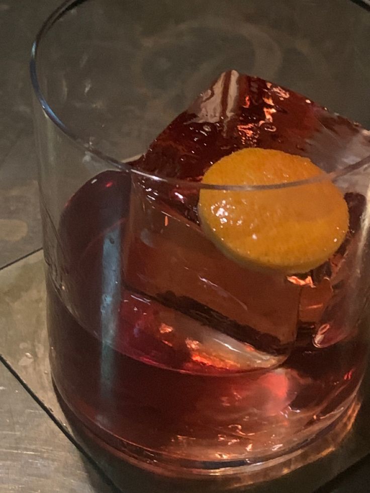 a glass filled with liquid and an orange slice on top of the ice cubes