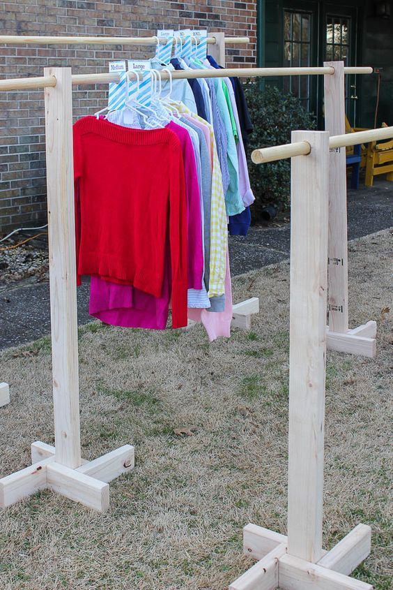 clothes are hanging on wooden racks in front of a brick building with grass and bushes