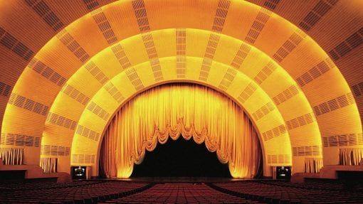 an empty auditorium with rows of seats and curtains on the walls, lit up by yellow lights