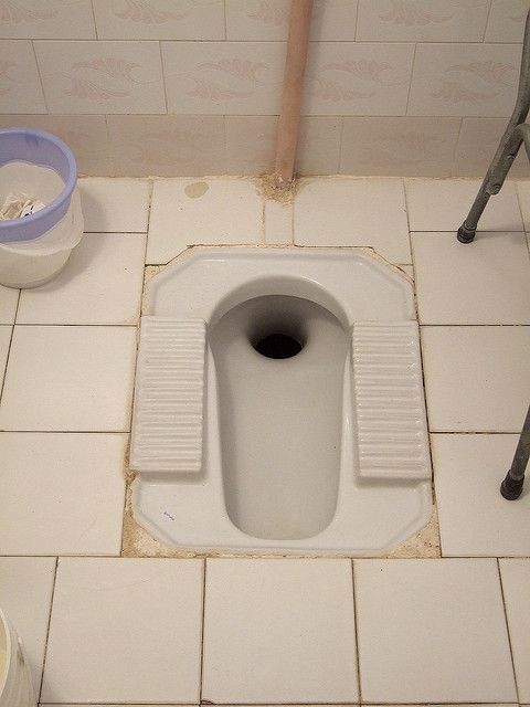 a white toilet sitting on top of a bathroom floor next to a bucket and plunger