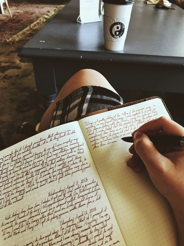 a person writing on a notebook with a cup of coffee in the backgroun