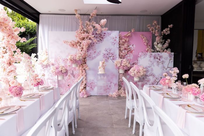 a table with white chairs and pink flowers on the wall behind it at a wedding reception