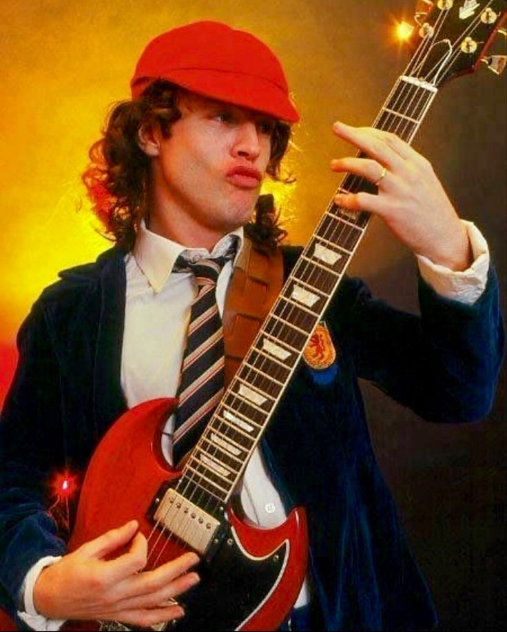 a man in a suit and tie holding an electric guitar with his right hand on the neck