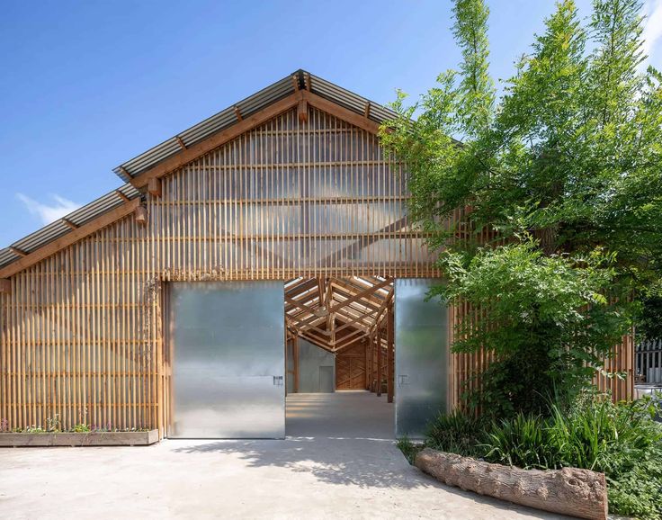 a large wooden building with an open door on the front and side walls, surrounded by greenery