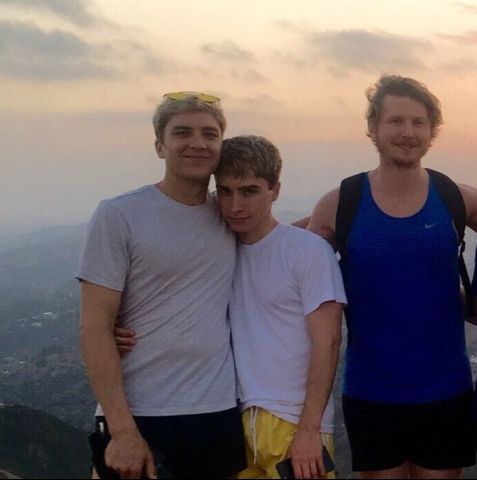 three young men standing on top of a mountain