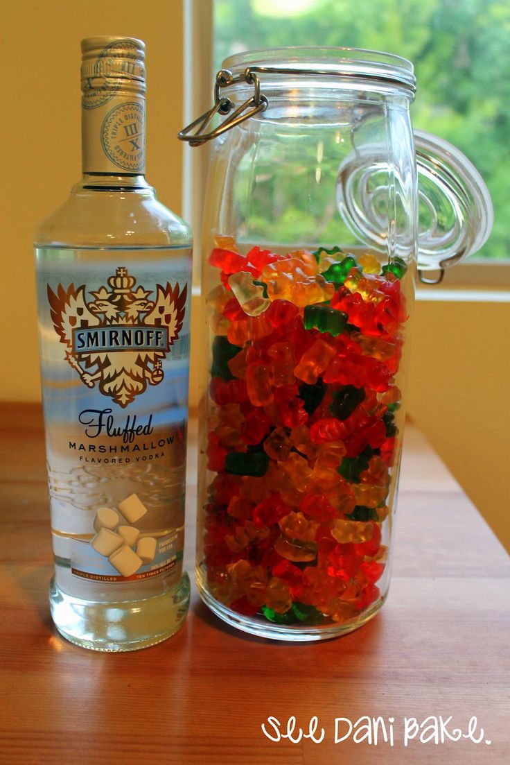 a glass jar filled with gummy bears next to a bottle of vodka