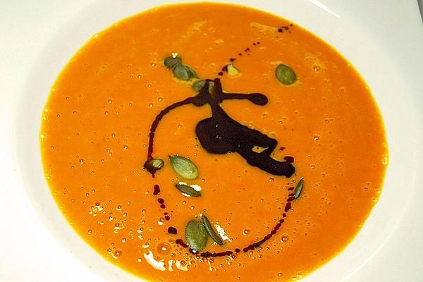 a white plate topped with a carrot soup and garnished with green leafy seeds