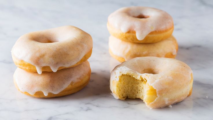 three glazed donuts with one missing and the other half open on a marble surface