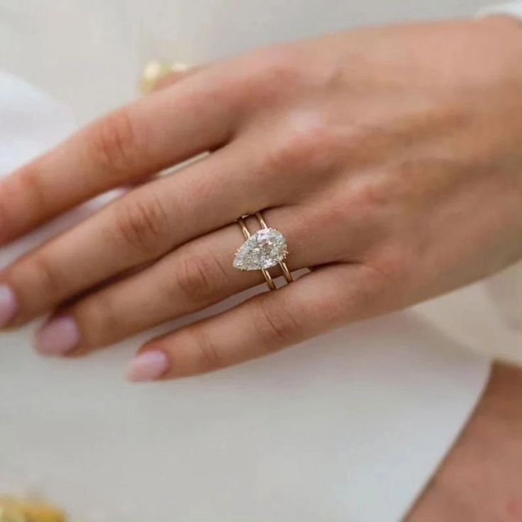 a close up of a person's hand wearing a ring with a pear shaped diamond