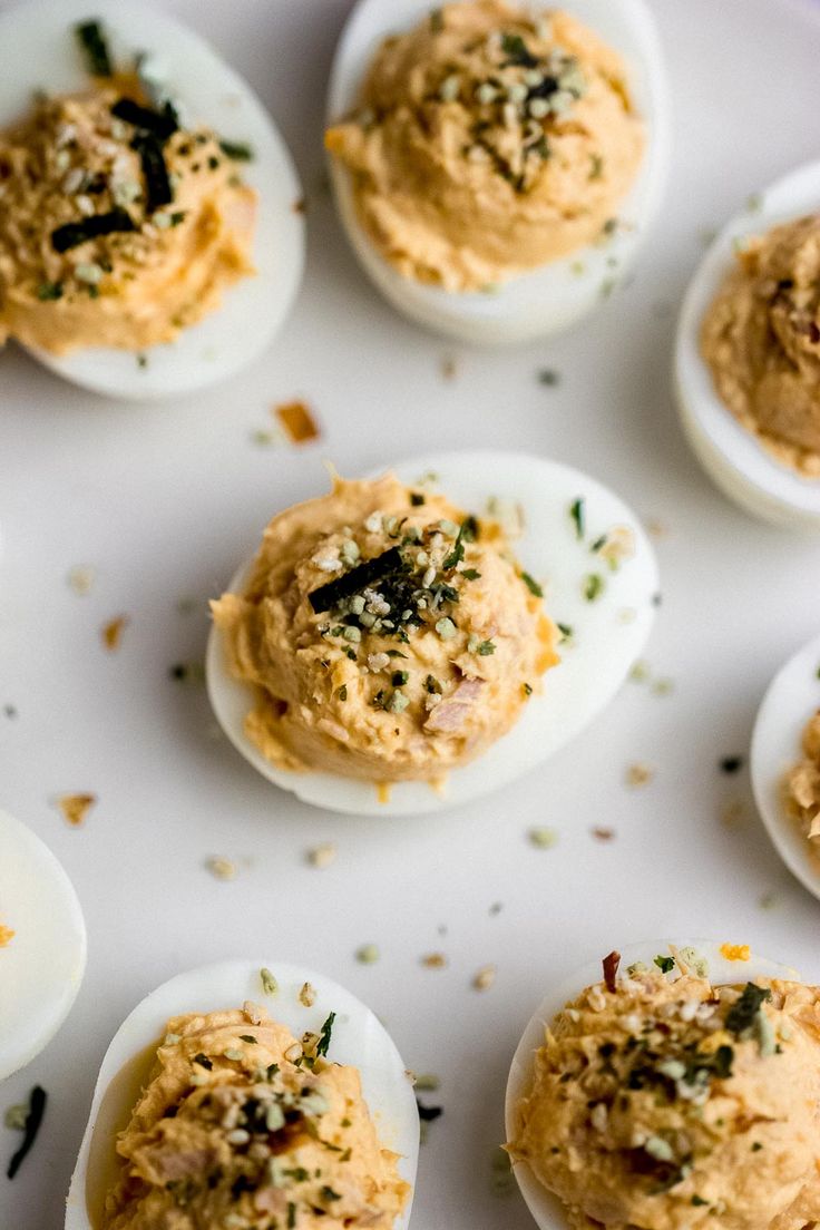 several deviled eggs with different toppings on a white plate, ready to be eaten