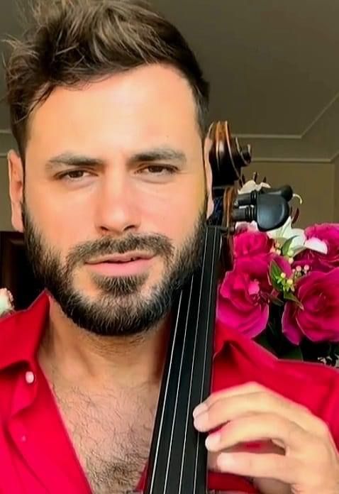 a man with a beard holding a violin in front of pink flowers and a vase