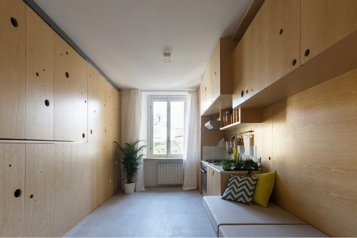 a long narrow kitchen with wooden cabinets and white counter tops, along with a bench in front of the window