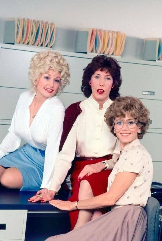 three women sitting on a desk in an office