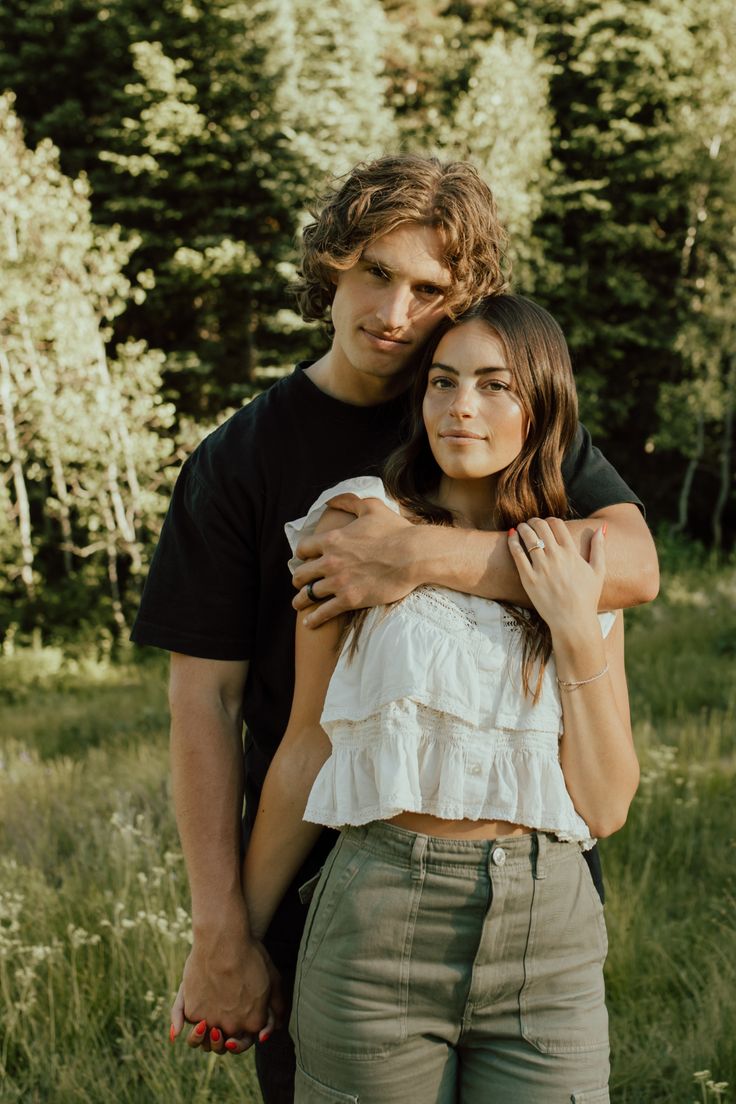 a young man and woman embracing in the woods