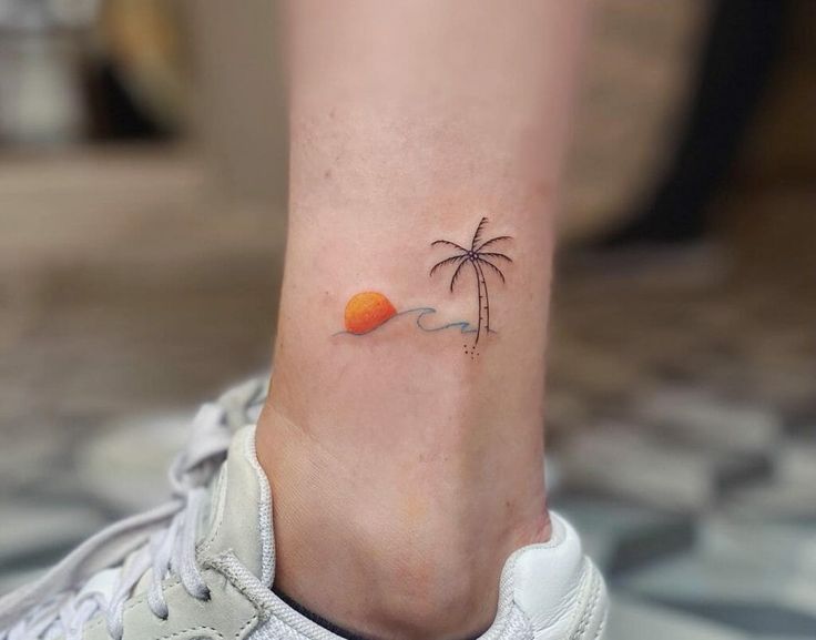 a small tattoo on the ankle of a woman with an orange ball and palm tree