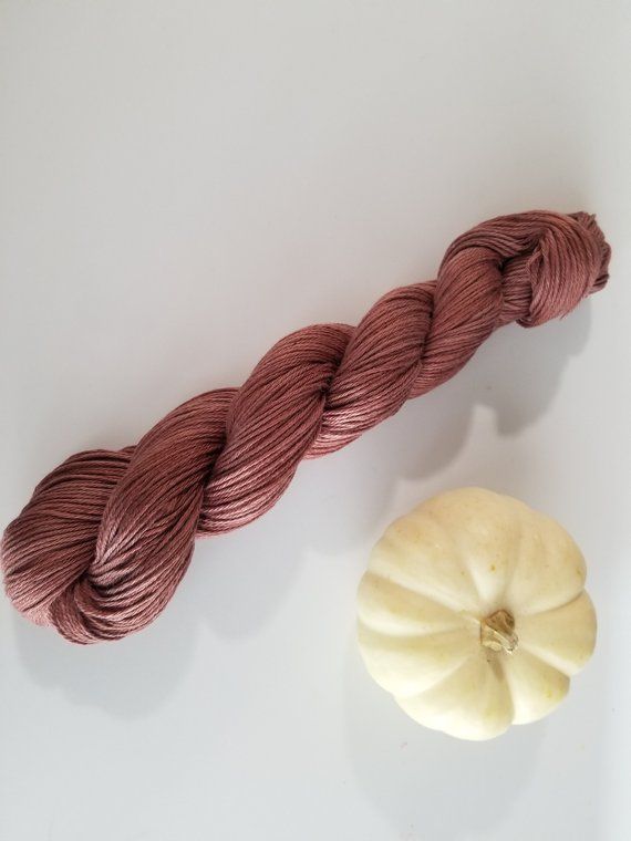 two skeins of yarn next to a pumpkin on a white surface with one spool in the foreground