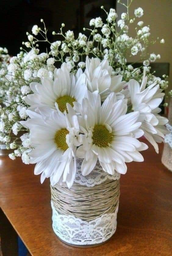 white flowers are in a vase on a wooden table with lace and twine around the edges