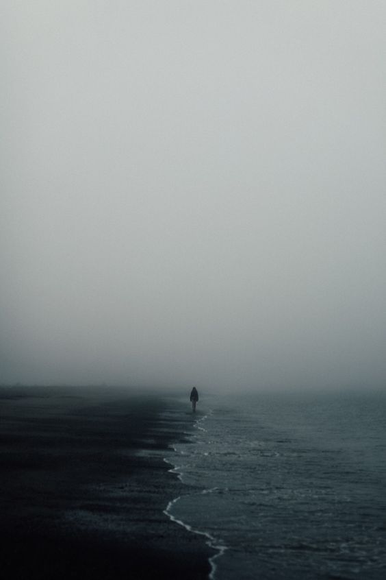 a lone person standing in the ocean on a foggy day