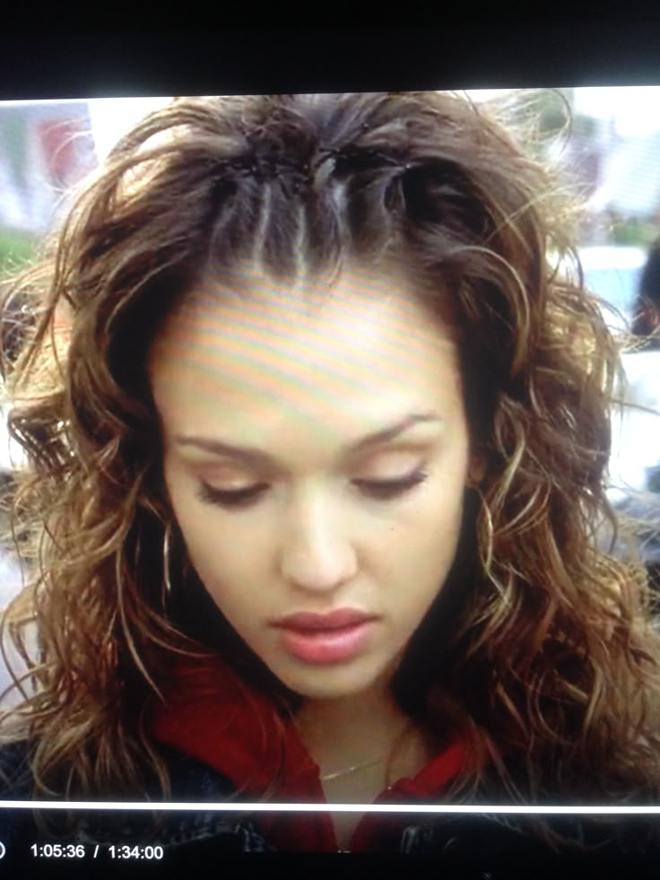 a woman with long hair looking down at her cell phone screen while she is on the street