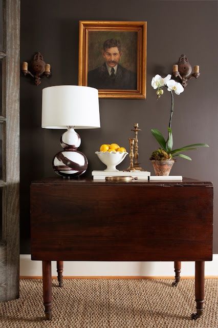 a living room with a table, lamp and pictures on the wall above it in front of a painting