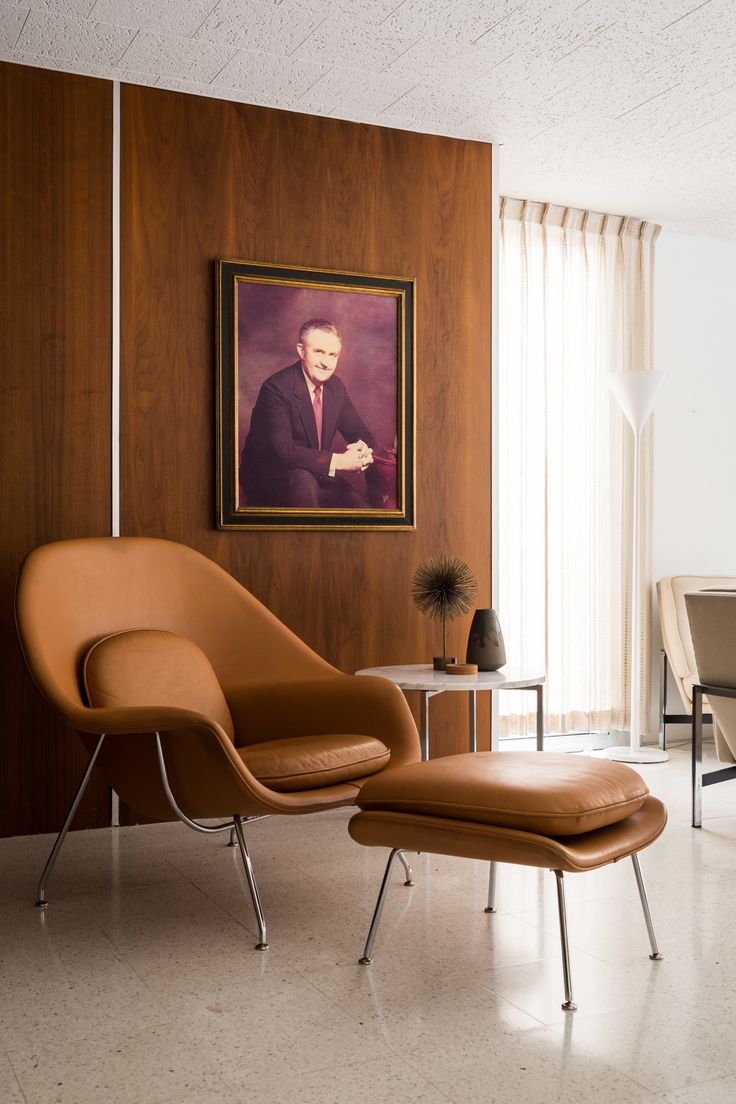 a chair and ottoman in front of a painting on the wall with a table next to it