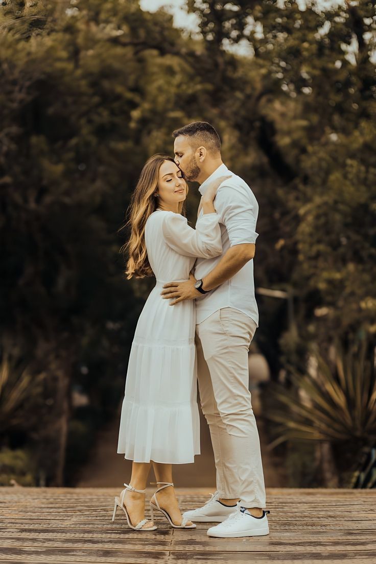 a man and woman standing next to each other on a wooden floor with trees in the background